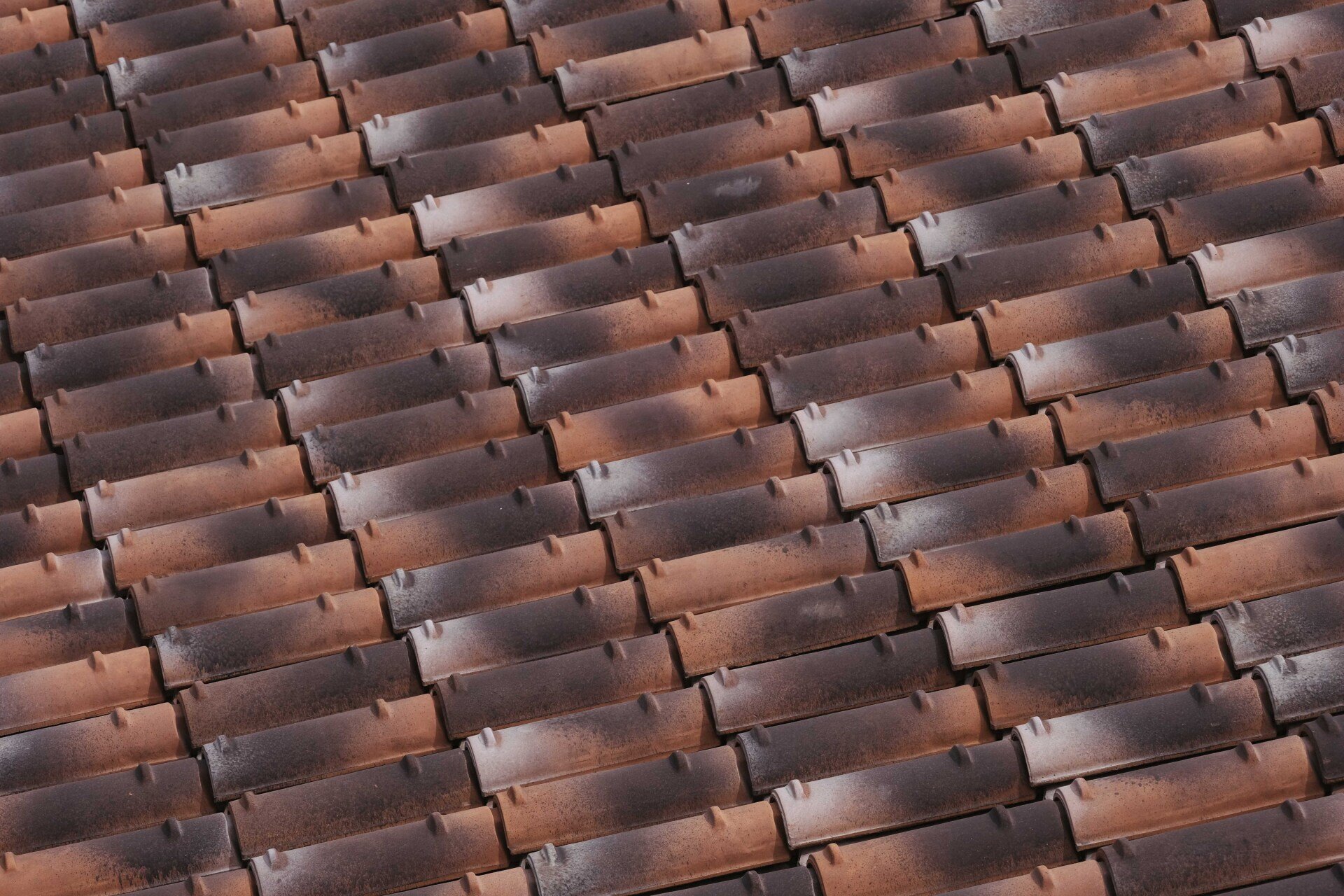 Detalle de filas de tejas superpuestas en tonos rojizos y marrones, con zonas oscuras en la superficie.
